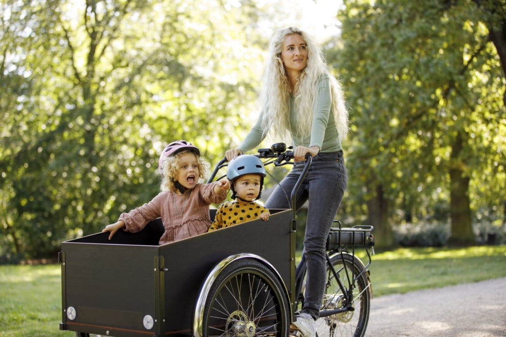 Mor som sykler med barna i sykkelvogn