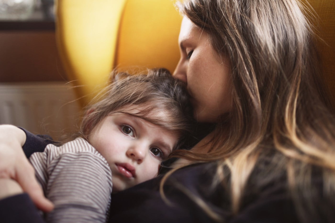 Mor kysser datteren sin på pannen mens de sitter i en komfortabel lenestol.