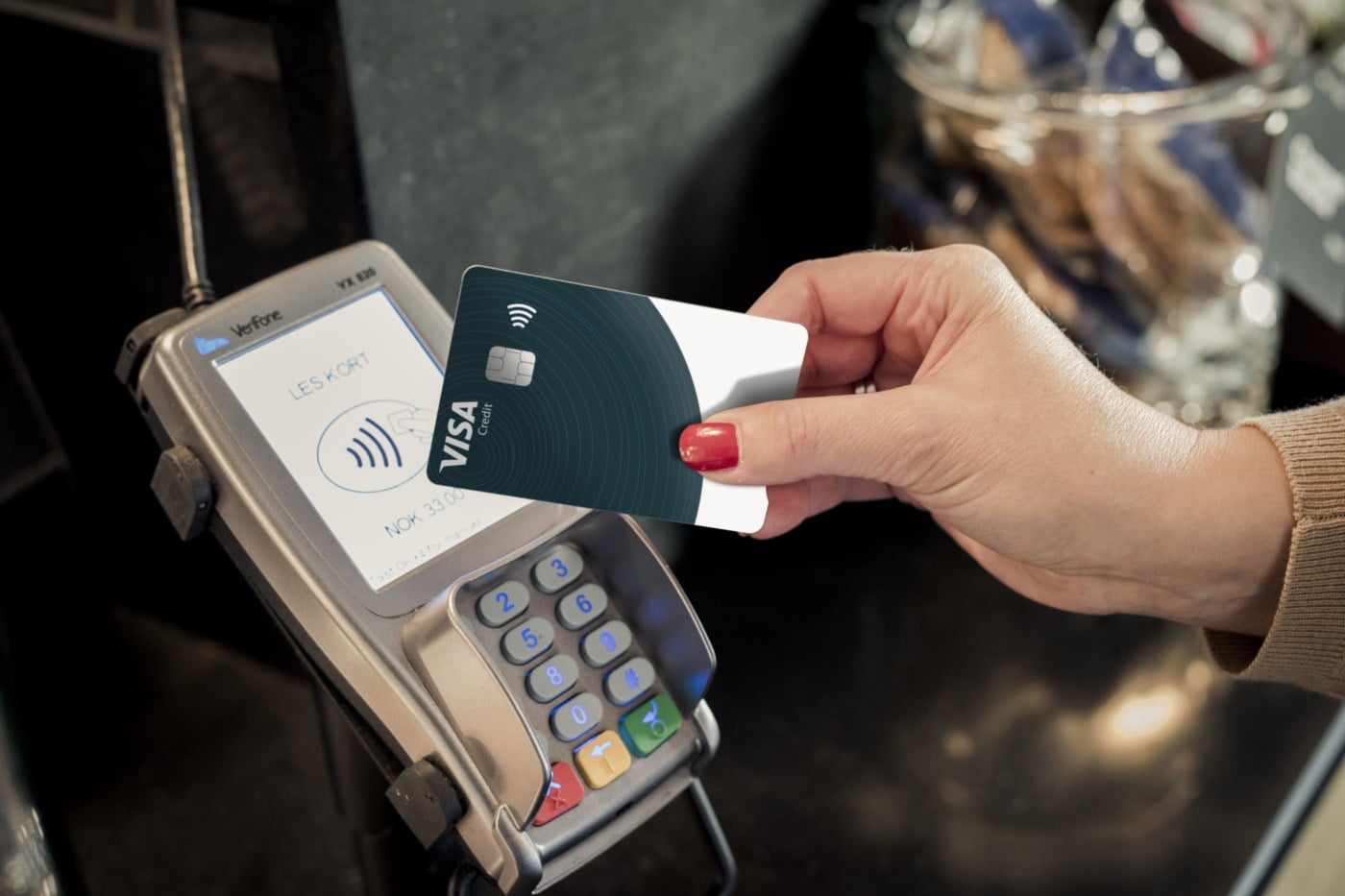 To handleposer med matvarer og mynter som flyr mot et Visa-kredittkort på blå bakgrunn.