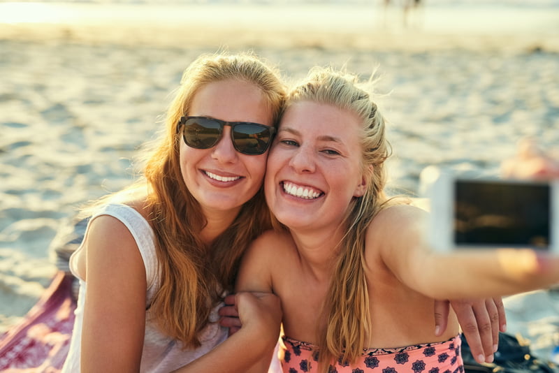 Jenter tar selfie på stranda en solfylt dag.