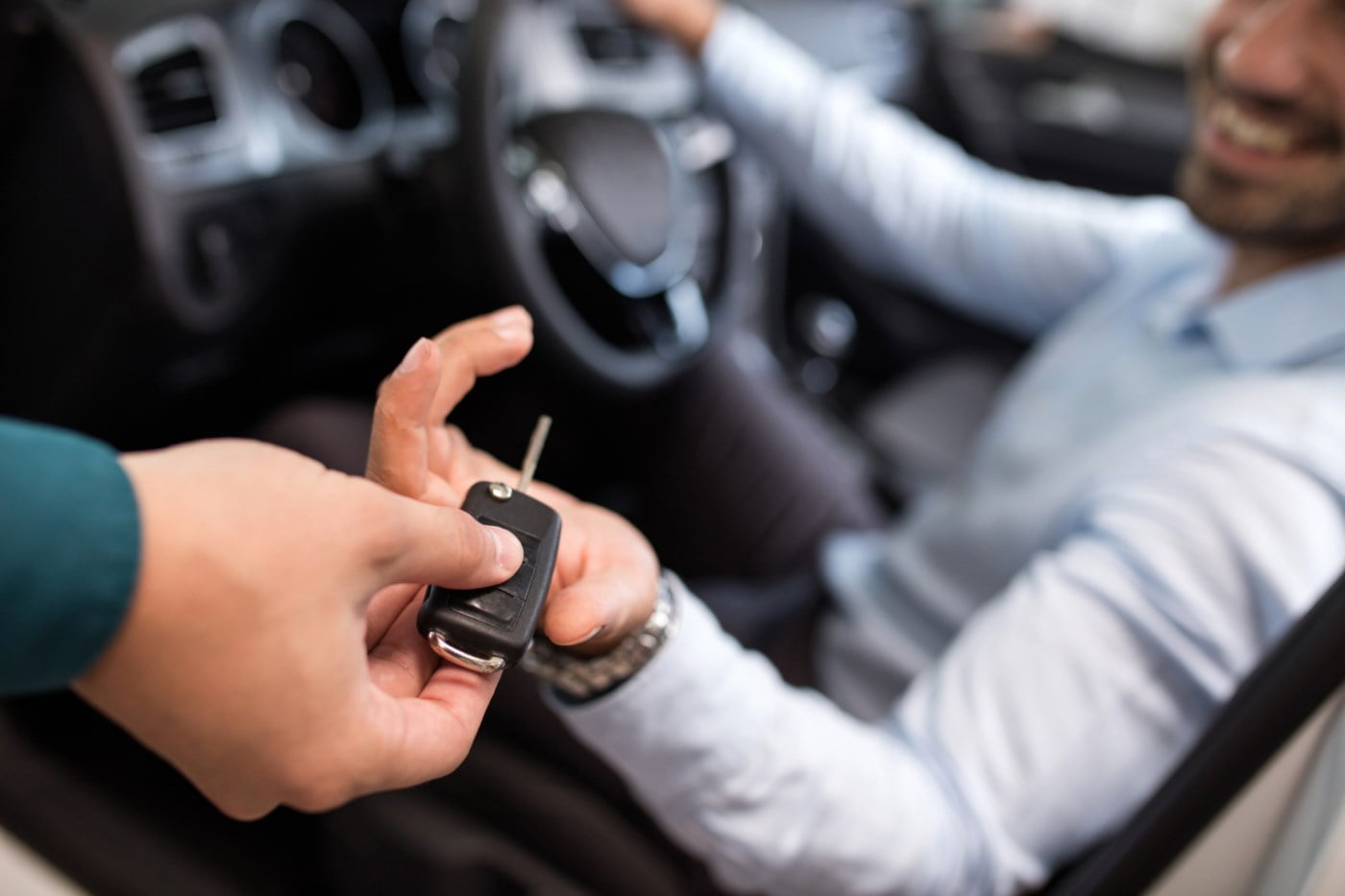En person overrekker bilnøkler til en annen person inne i en bil, symboliserer starten på en ny kjøreopplevelse.