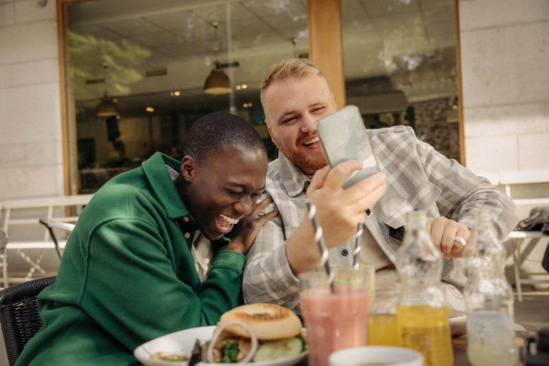 To gutter sitter p restaurant med mobil og smiler og ler