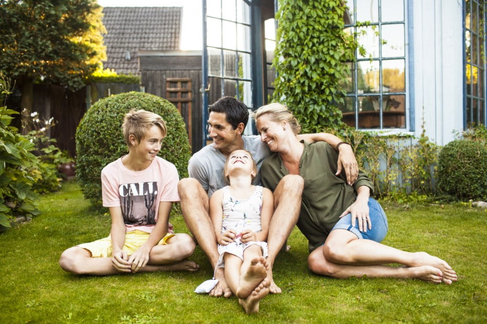 Familie med to barn som sitter på gresset ute i hagen en sommerkveld