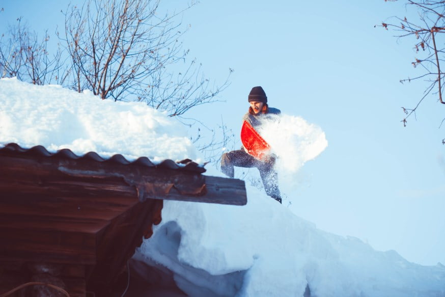 Mann måker snø fra tak. Foto. 